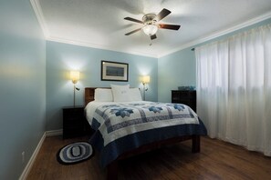 Ein Schlafzimmer mit einem Bett, zwei Nachttischlampen, einem Deckenventilator, einem gerahmten Bild und einem Nachttisch.