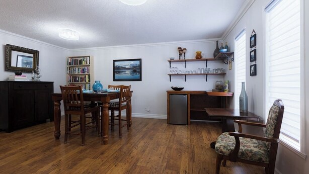 Un comedor con mesa y sillas de madera, una estantería, un refrigerador y una ventana con persianas.
