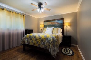 A bedroom with a bed, a ceiling fan, a painting on the wall, and two bedside lamps.