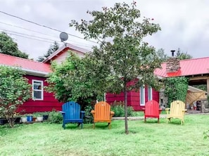 Una casa roja con chimenea, un árbol y cuatro sillas Adirondack en el frente.