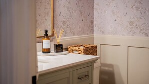 A bathroom with a white vanity, a bottle of hand soap, reed diffusers, and a woven basket. - Queens Hall, Historic Luxury in St. John's (St. John's)