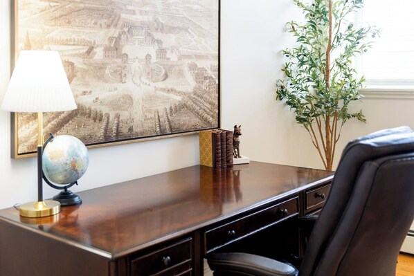 A desk with a globe, books, and a statue, a lamp, and a large framed picture on the wall.