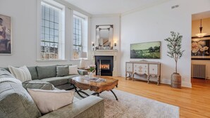 A living room with a fireplace, a sofa, a coffee table, and a television. - Queens Hall, Historic Luxury in St. John's (St. John's)