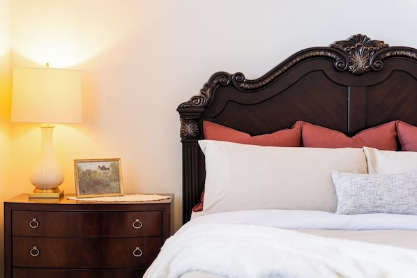 A neatly made bed with a dark headboard, a bedside lamp, and a small bedside table with a picture frame.