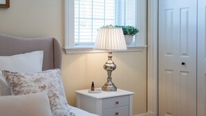 A bedroom with a bed, a bedside table with a lamp, a window with blinds, and a door. - Queens Hall, Historic Luxury in St. John's (St. John's)