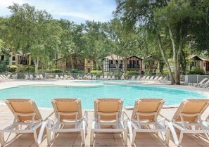 A swimming pool with lounge chairs and wooden cabins in the background.