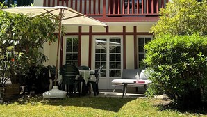 Edificio de dos pisos con balcón, asientos al aire libre y un jardín.