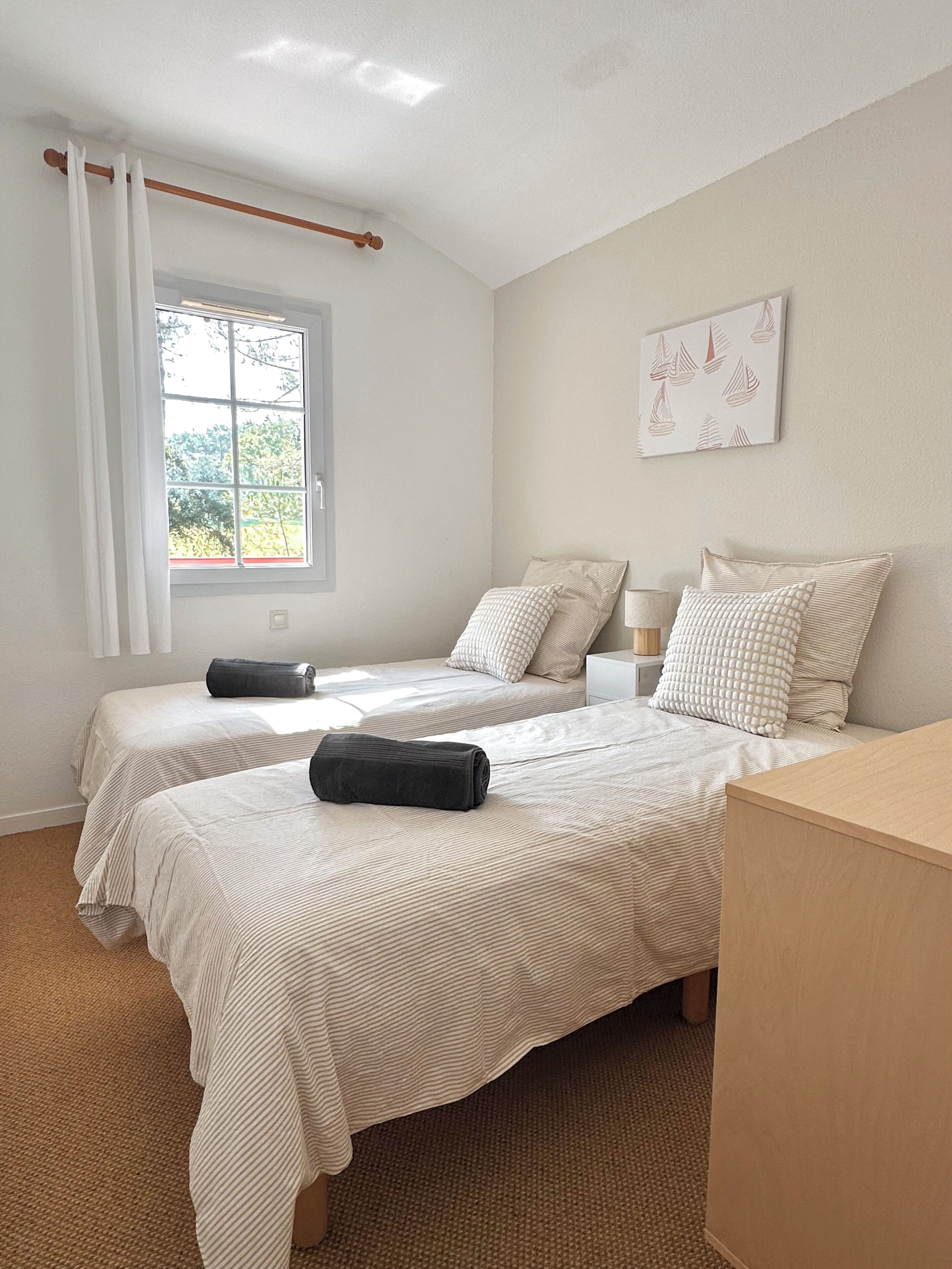 Une chambre avec deux lits, une fenêtre avec des rideaux, une table de chevet et une œuvre d’art accrochée au mur.