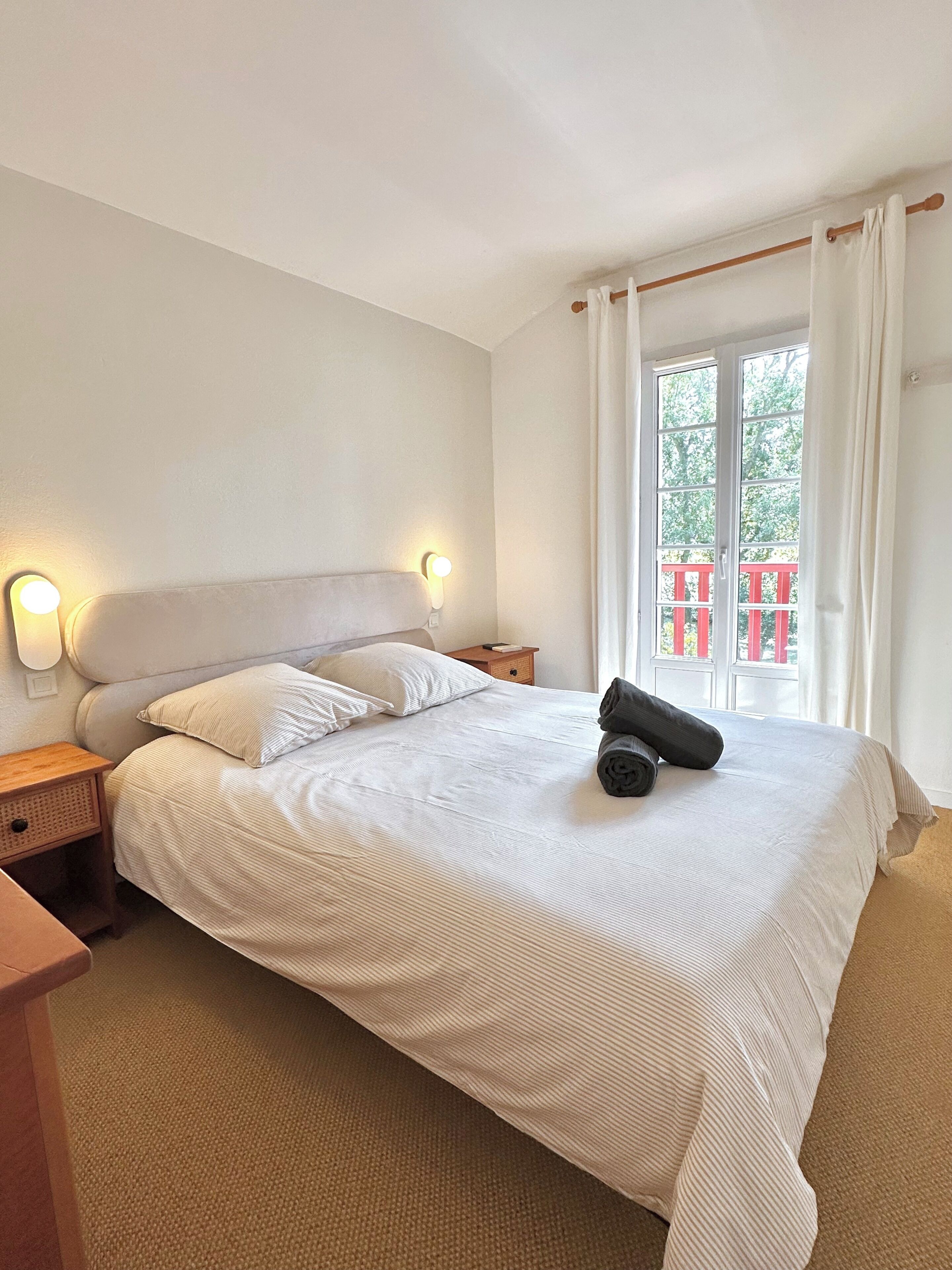 Ein Hotelzimmer mit Bett, Nachttischen, Vorhängen vor einem Fenster und Blick auf einen Balkon.