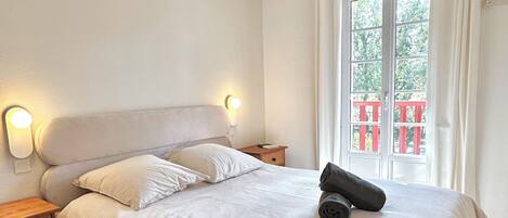Ein Hotelzimmer mit Bett, Nachttischen, Vorhängen vor einem Fenster und Blick auf einen Balkon.