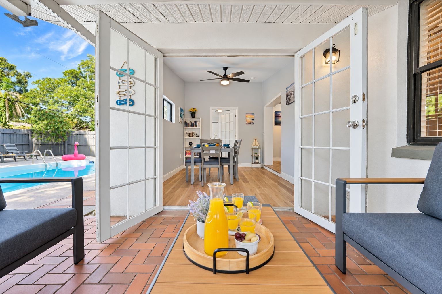 Une terrasse ouverte avec une piscine, un coin repas et un espace détente agrémenté d’un plateau de jus d’orange et de fruits.