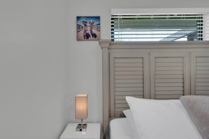 A hotel room with a bed, a nightstand with a lamp, a painting on the wall, and a window with blinds. - Pool, Fire Pit, Near Beaches | Sleeps 9, Dogs OK (Largo)