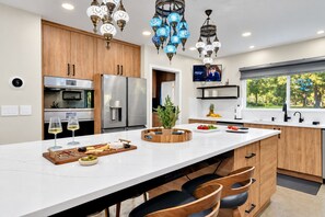 A modern kitchen with a large island, stainless steel appliances, and decorative blue hanging lights. - Casa Lumina | 8 Bedroom Luxury Estate | Pool, Spa & Outdoor Kitchen (Temple Terrace)