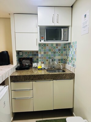 A compact kitchen with a microwave, sink, and a tiled backsplash. - Marinas Flat 005 | Your beachfront retreat in Cabo Branco with your family. (João Pessoa)