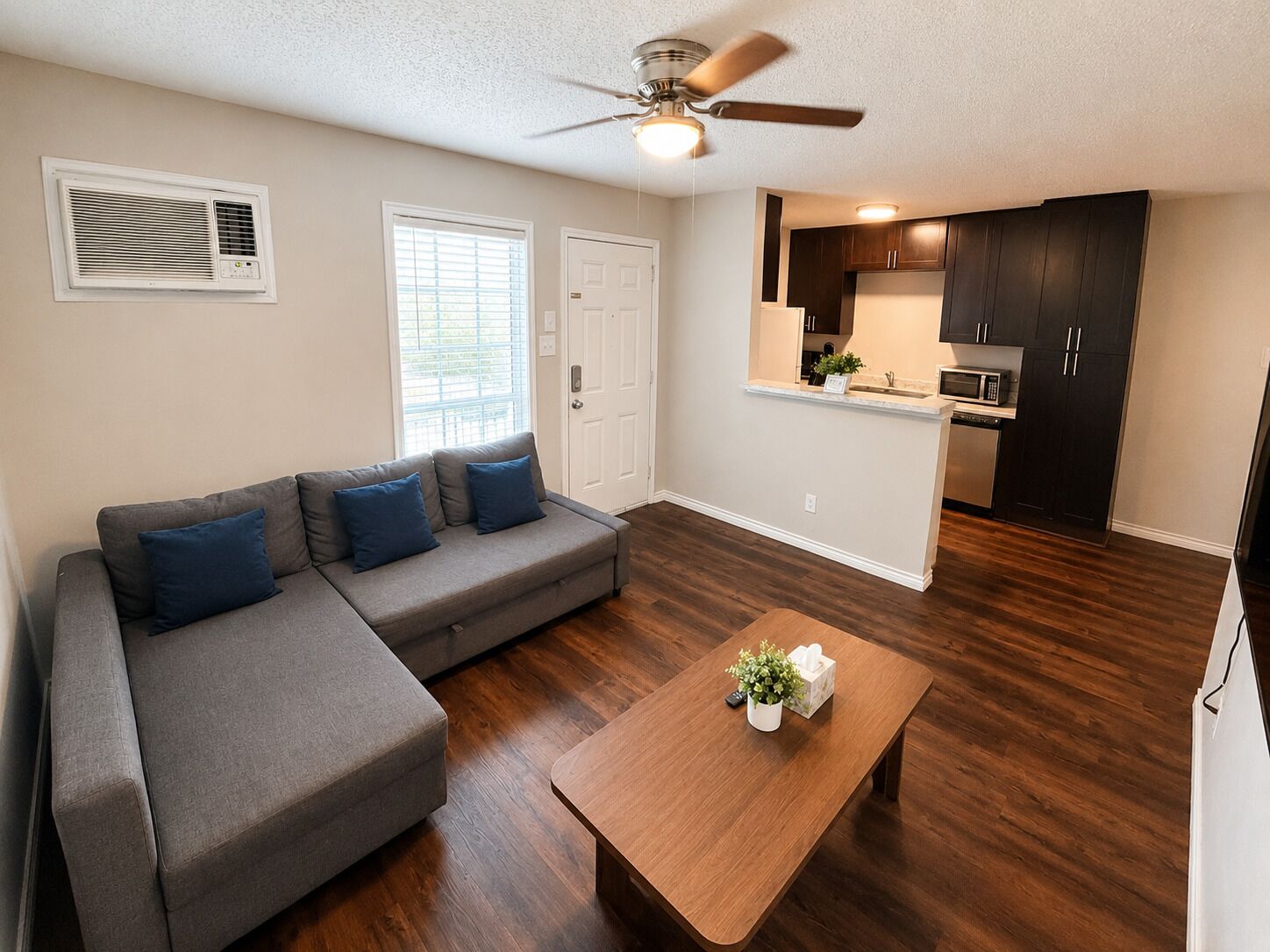 A living room with a gray sectional sofa, a wooden coffee table, and a ceiling fan.
