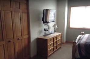 A bedroom with a wooden wardrobe, a television mounted on the wall, a bedside table with a lamp, and a window providing natural light. - Great Location. On bus route with private hot tub. Sleeps 9. Great, comfy place! (Breckenridge)
