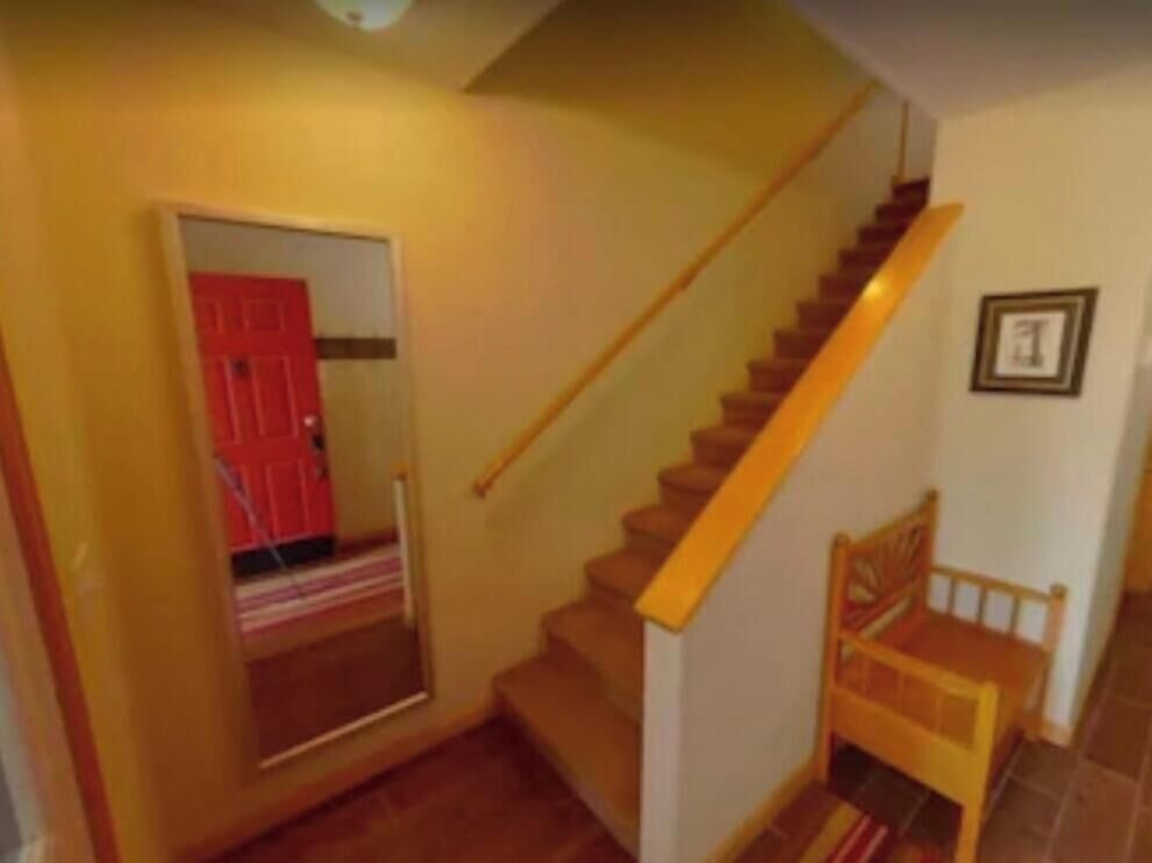 A staircase with a wooden handrail and a red door at the bottom.