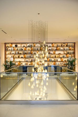 Un interior moderno con una lámpara central, barandilla de cristal y una estantería llena de libros.