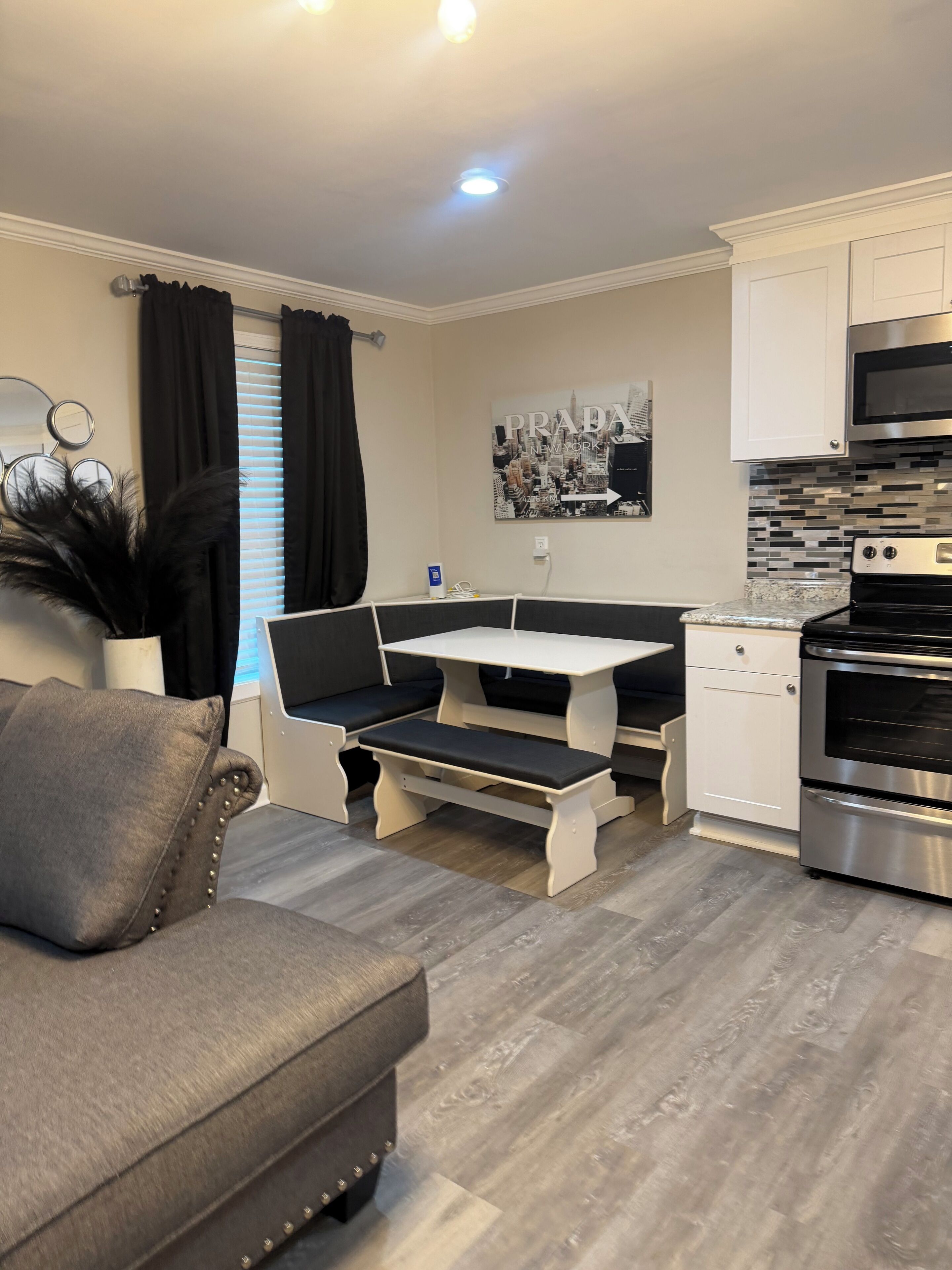 A compact kitchen with a built-in oven, a dining table with benches, and a grey sofa.