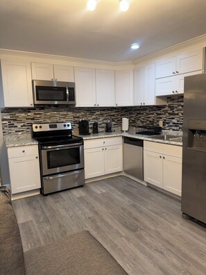 A modern kitchen with white cabinets, stainless steel appliances, a tiled backsplash, and a wooden floor. - Cozy 1-bedroom apartment in delightful Jonesboro with AC (Jonesboro)