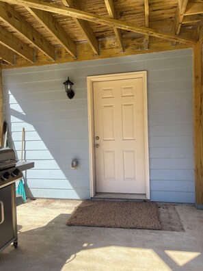 A wooden ceiling with metal brackets, a white door, and a concrete floor with a doormat. - Cozy 1-bedroom apartment in delightful Jonesboro with AC (Jonesboro)