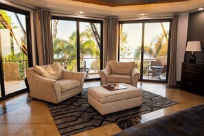 Amplia sala de estar con dos sillones, una mesa de centro y vistas al exterior a través de amplias puertas correderas de cristal.
