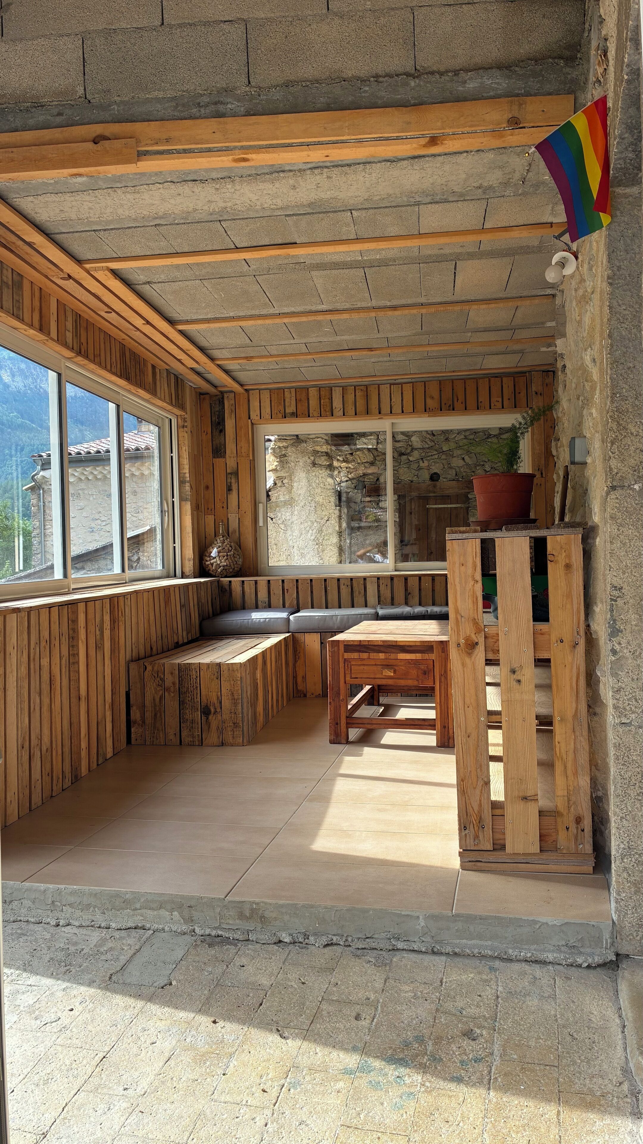 A rustic interior with wooden walls, a stone bench, and a view of the outside.