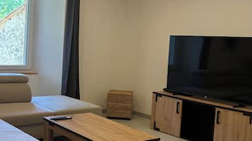 A modern living room with a sofa, a wooden coffee table, a television on a wooden stand, and a window with curtains.