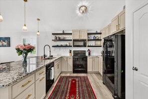 A modern kitchen with a marble countertop, stainless steel appliances, and a red patterned rug.