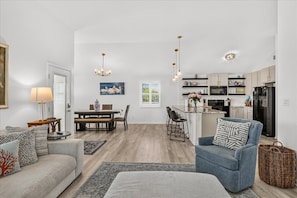 A modern living room with a sofa, armchair, and dining table. There is a kitchen in the background with cabinets and appliances. - NEW|Large, Private Pool|Pets Welcome! (Port Aransas)