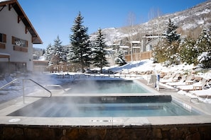 Uma área de hidromassagem com parede de pedra, espreguiçadeiras e piscina.