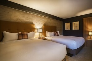 Ett hotellrum med två sängar, en sänggavel i trä, ett nattduksbord med en lampa och inramade konstverk på väggen.