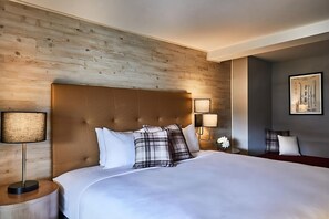 Ein Hotelzimmer mit einem hölzernen Kopfteil, einem großen Bett mit weißer Bettwäsche, zwei Nachttischlampen und einem gerahmten Bild an der Wand.