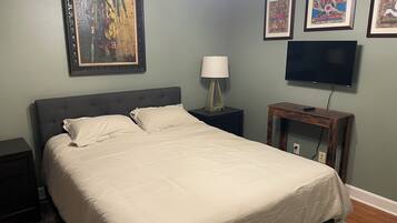 Un dormitorio con cama, mesita de noche, lámpara, televisor y cuadros en la pared.