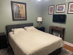 Un dormitorio con cama, mesita de noche, lámpara, televisor y cuadros en la pared.