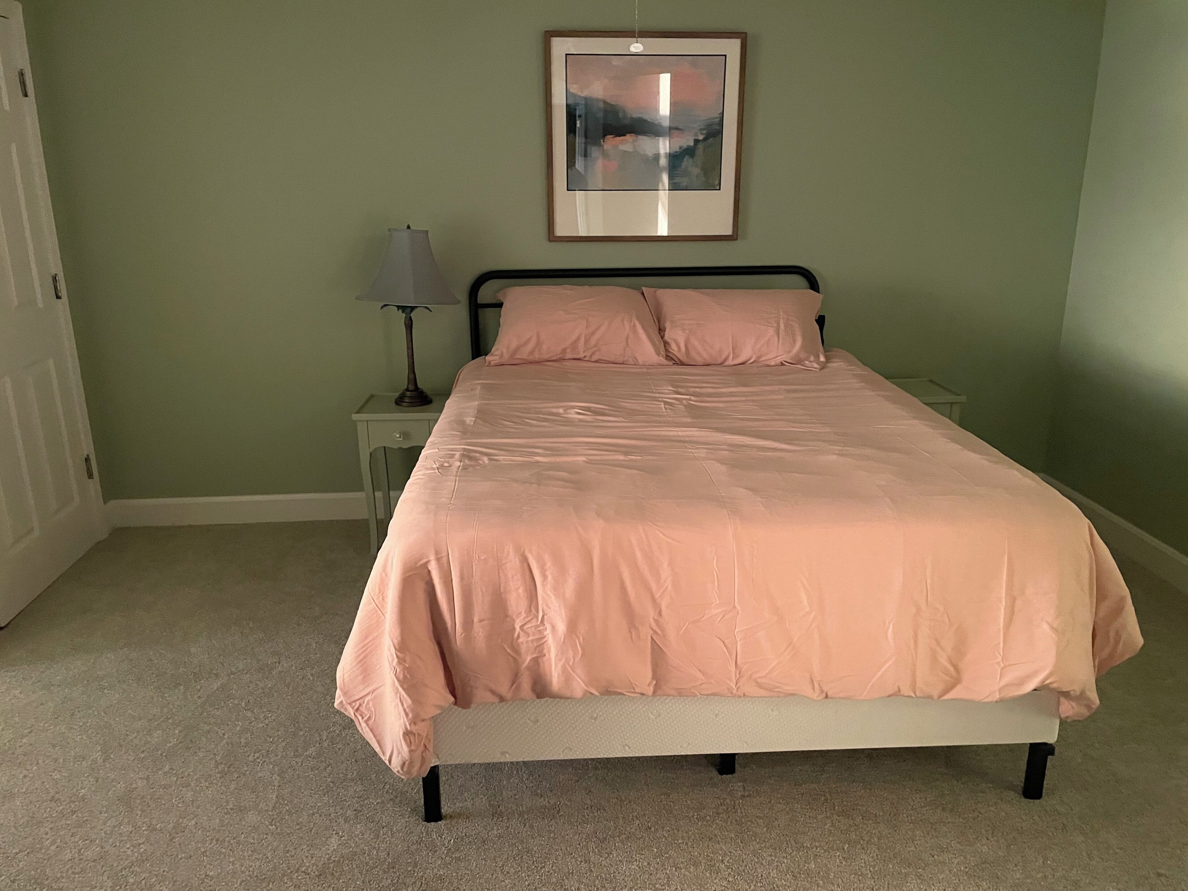 A bedroom with a bed, a nightstand, a lamp, and a framed picture on the wall.