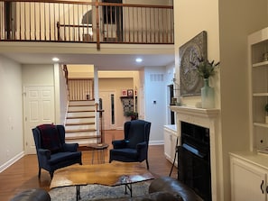 A spacious living room with a fireplace, a staircase leading to an upper level, and a view of the outdoors.