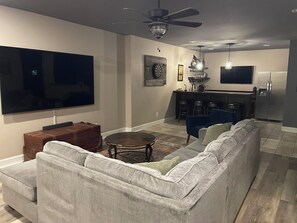 A living room with a large flat-screen TV, a sofa, a coffee table, and a ceiling fan.
