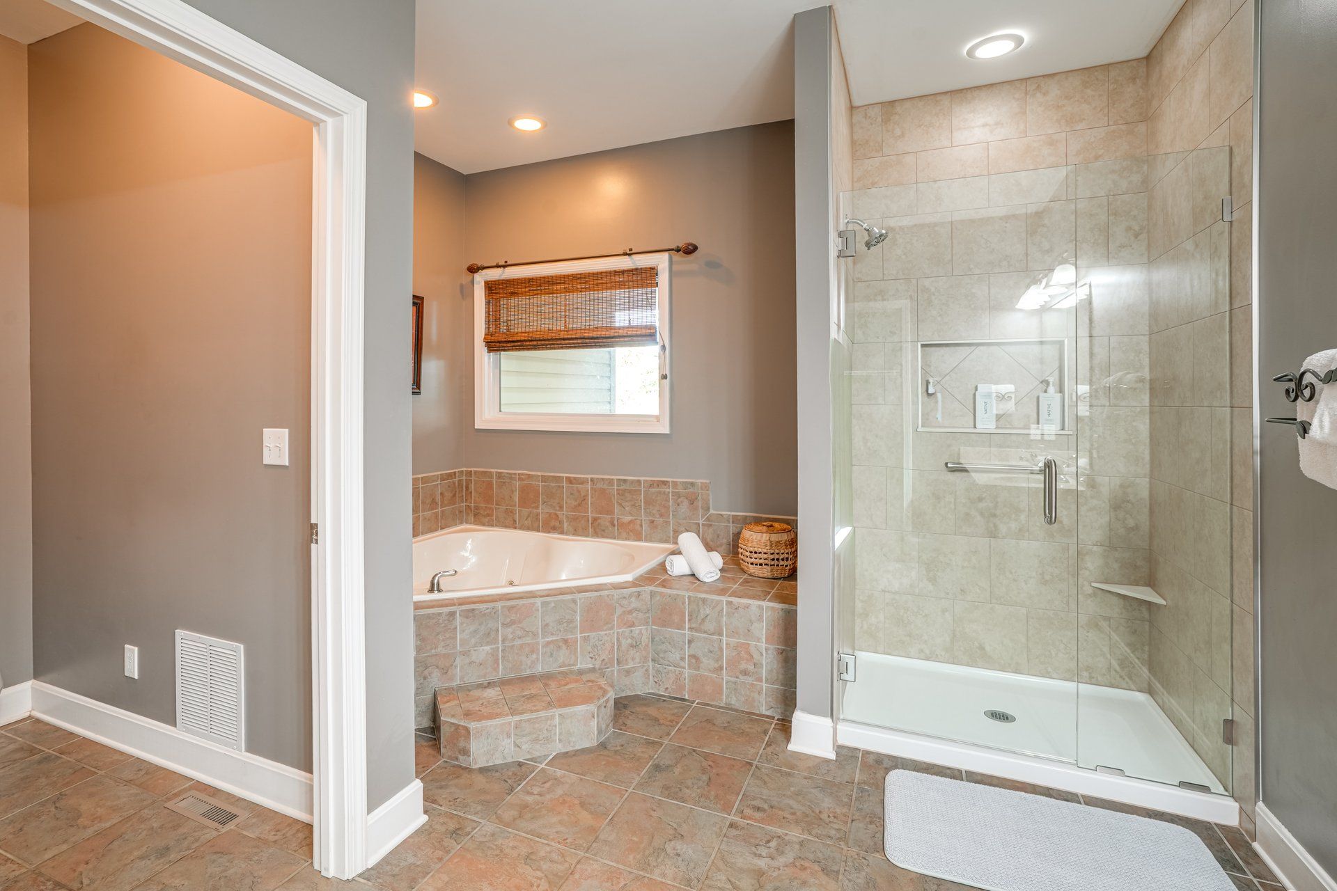 A bathroom with a walk-in shower, a bathtub, and a window with a blind.