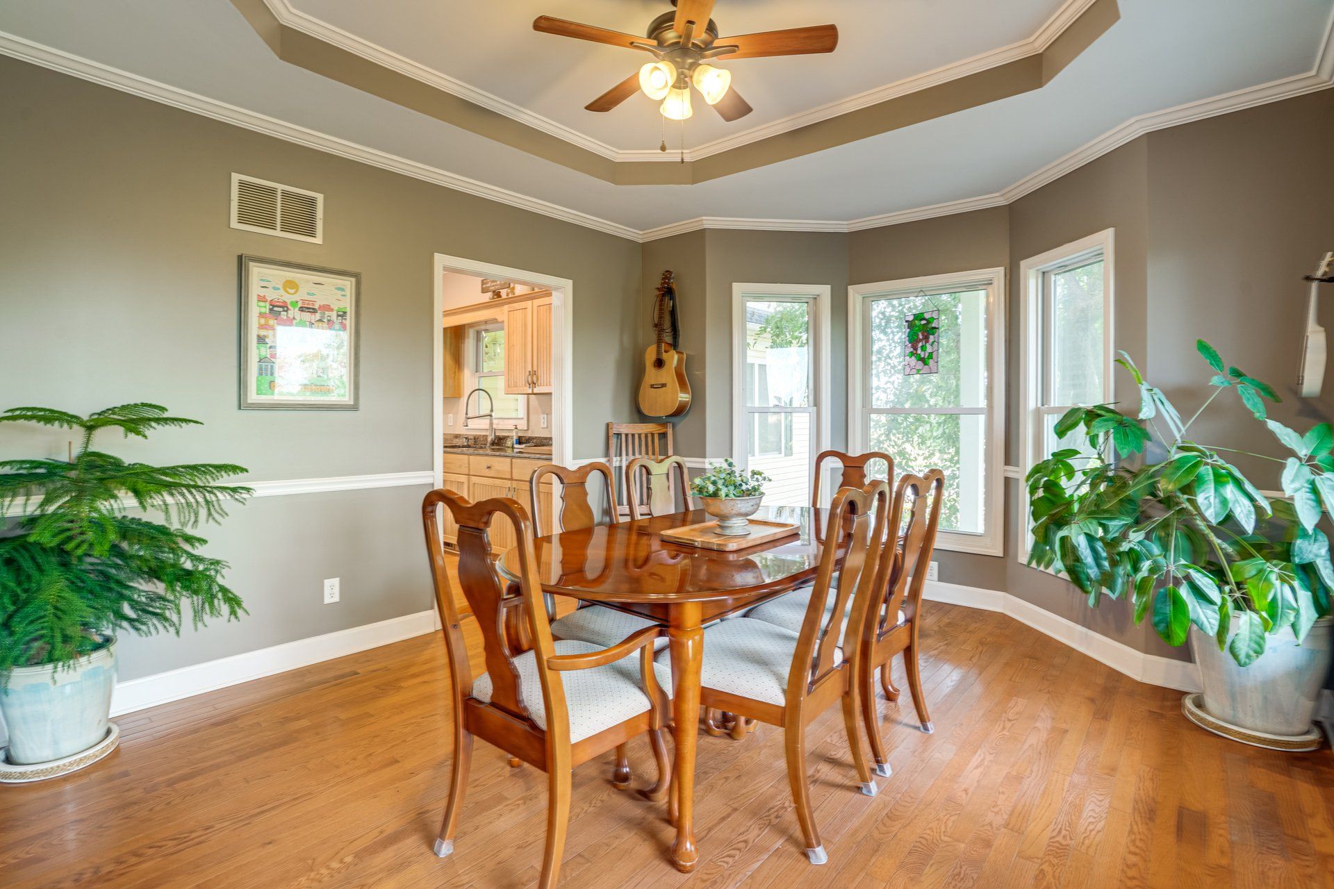 A dining room with a wooden table and chairs, a ceiling fan, and large windows.
