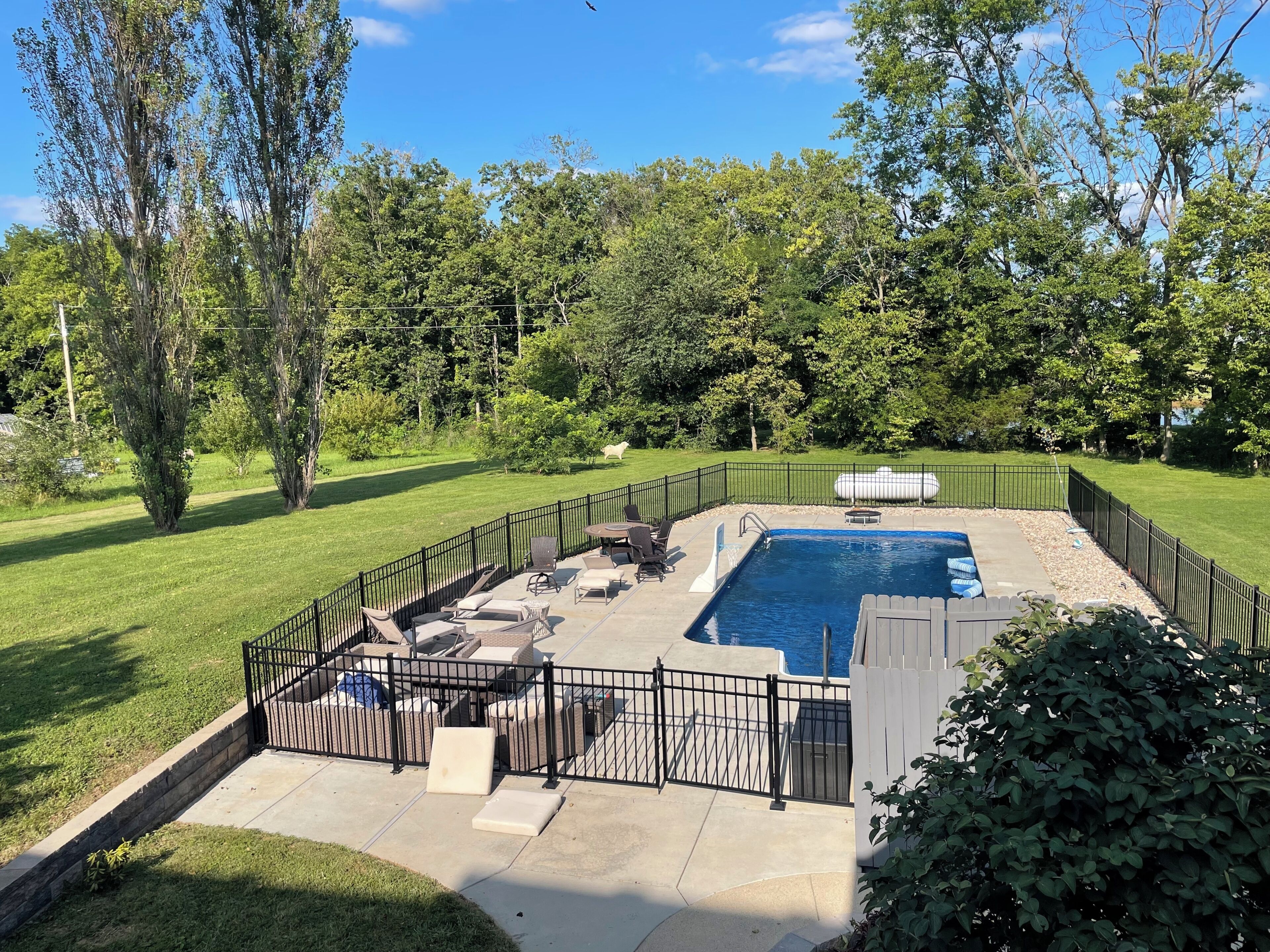 A backyard with a swimming pool, surrounded by a fence, and a grassy lawn.
