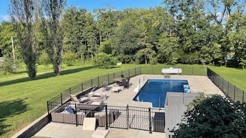 A backyard with a swimming pool, surrounded by a fence, and a grassy lawn.