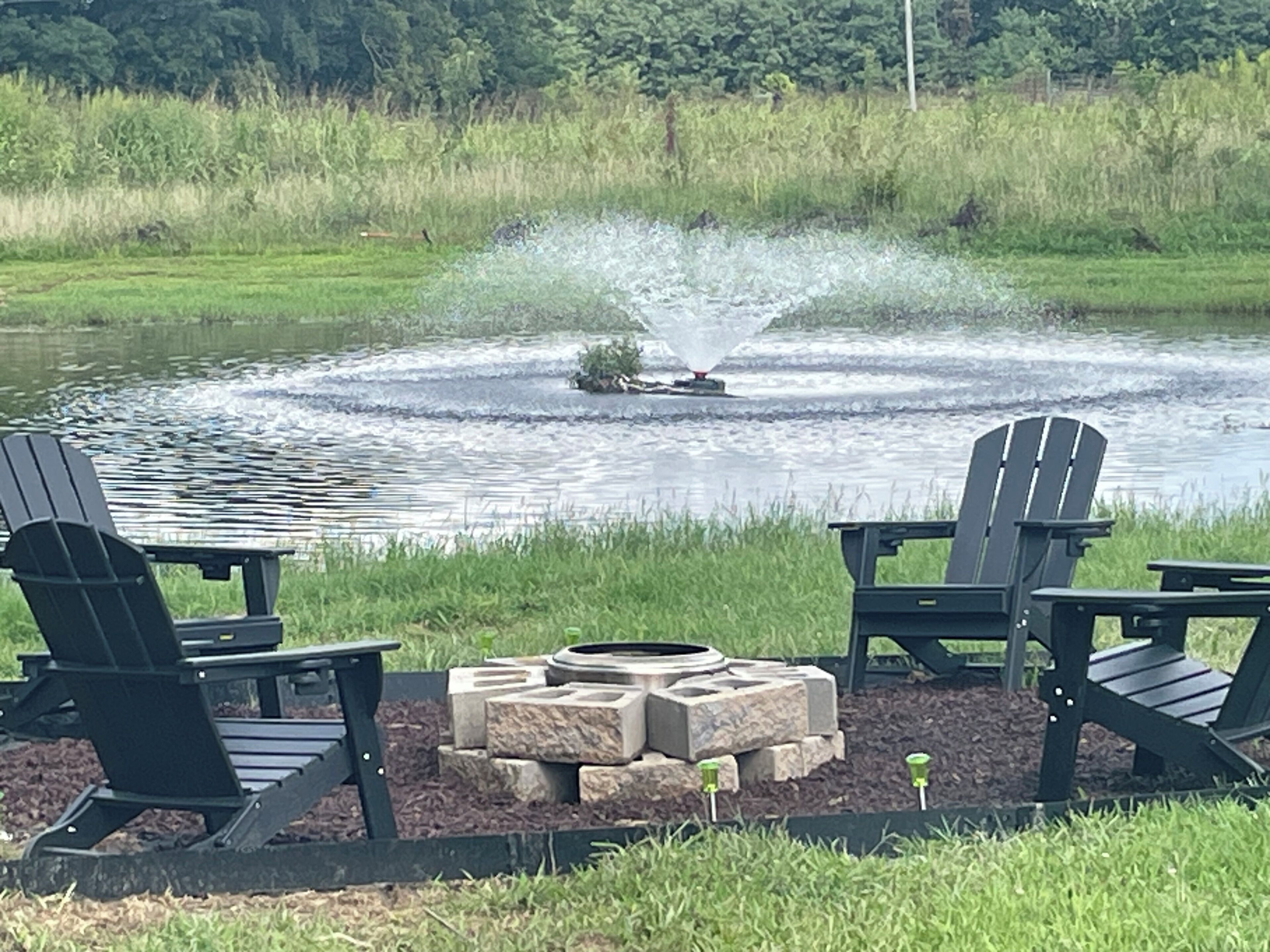 A lakeside seating area with Adirondack chairs and a fire pit.