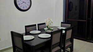 A dining area with a table set for four, chairs, a wall clock, and a ceiling light fixture.