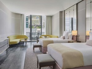 Ein Hotelzimmer mit zwei Betten, einem Sofa, einem Schreibtisch und Blick auf die Stadt.