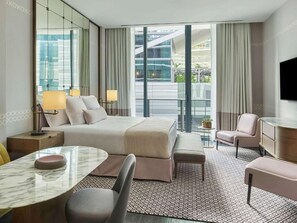 Ein modernes Hotelzimmer mit einem großen Bett, einem Schreibtisch mit Stuhl, einem kleinen Tisch und einem Fernseher.