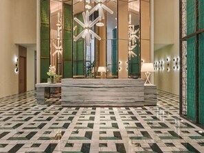 Eine Lobby mit einer Marmor-Rezeption, Fliesen mit Muster und modernen Leuchten.