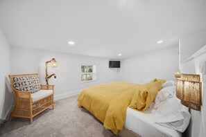 A bedroom with a bed, a chair, a television, and a window.