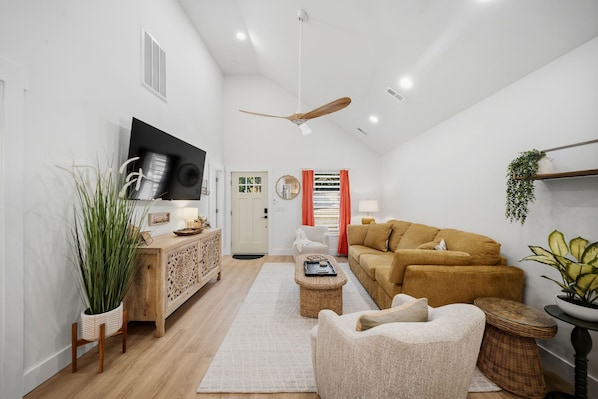 A modern living room with a flat-screen TV, a ceiling fan, a sofa, a coffee table, and a sideboard.