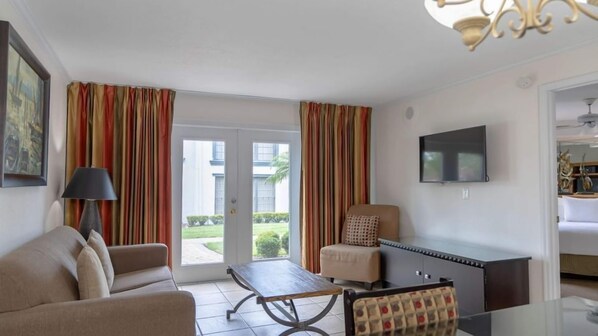 A living room with a sofa, a coffee table, a TV mounted on the wall, and a sliding door leading to an outdoor area. - One-Bedroom Suite w/ Living Room Near Orlando Fun (Orlando)